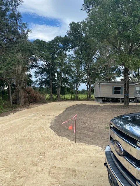 Graded driveway with compacted soil, mature trees, and cleared site preparation
