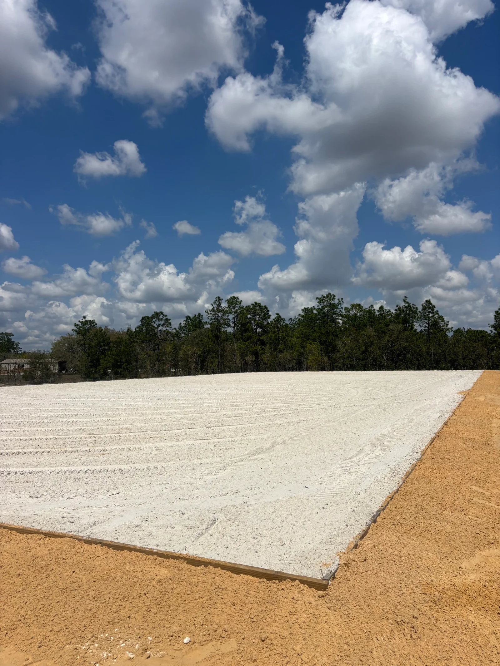 Graded site with crushed limestone base and staged earth material, tree line in background