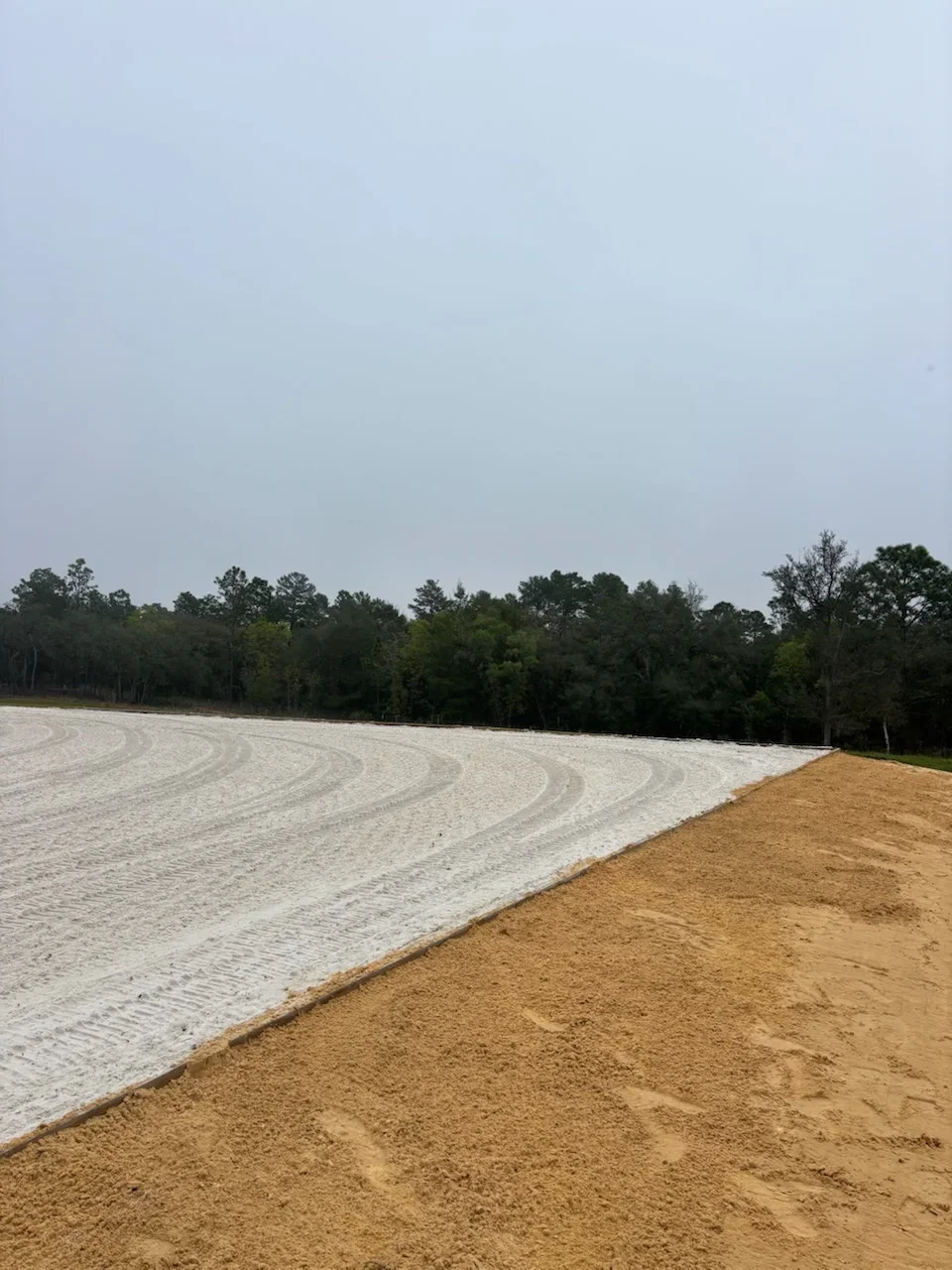 Cleared land with graded earth and white fabric erosion control, tree line in background